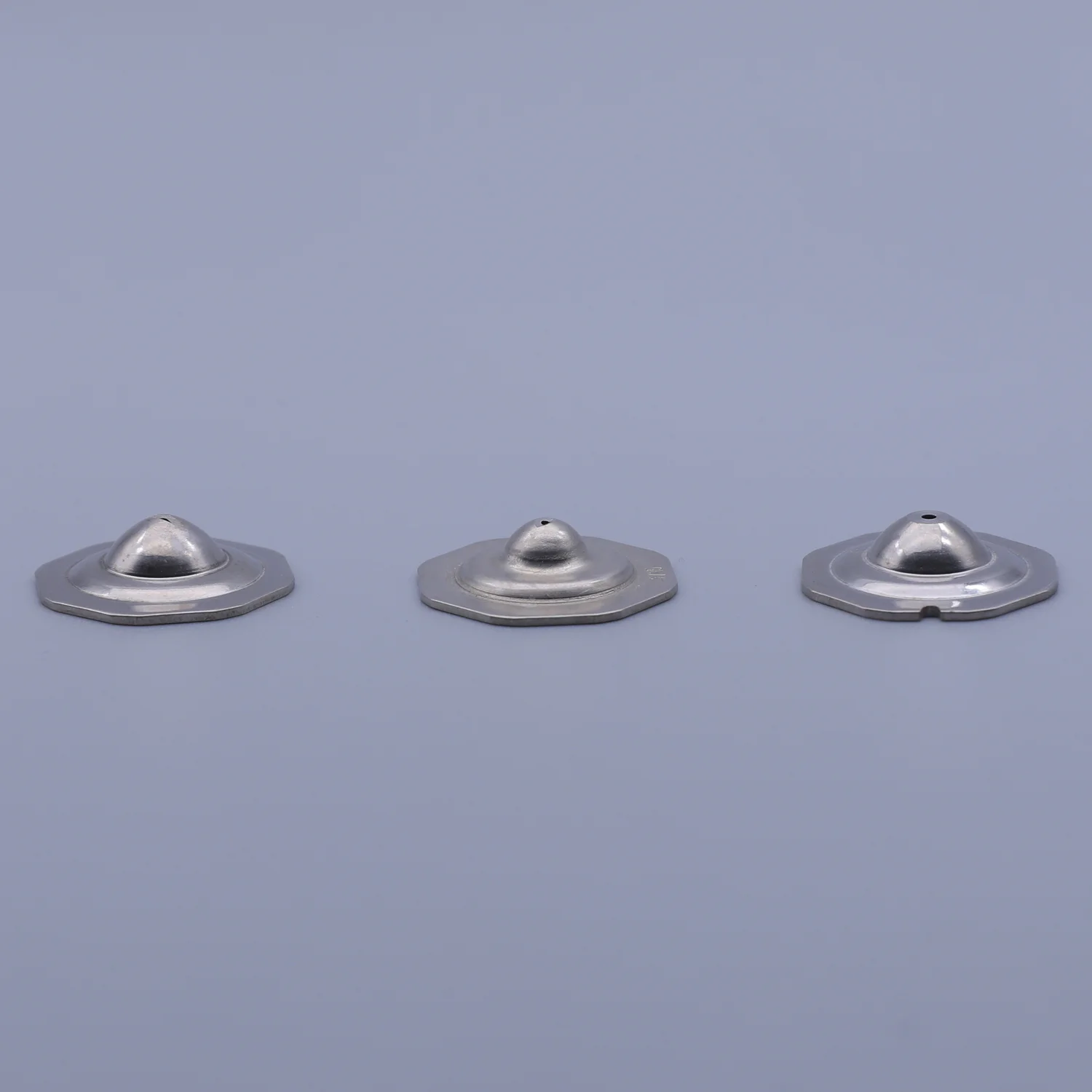 Three silver metallic components with circular bases and dome-shaped tops arranged on a plain background