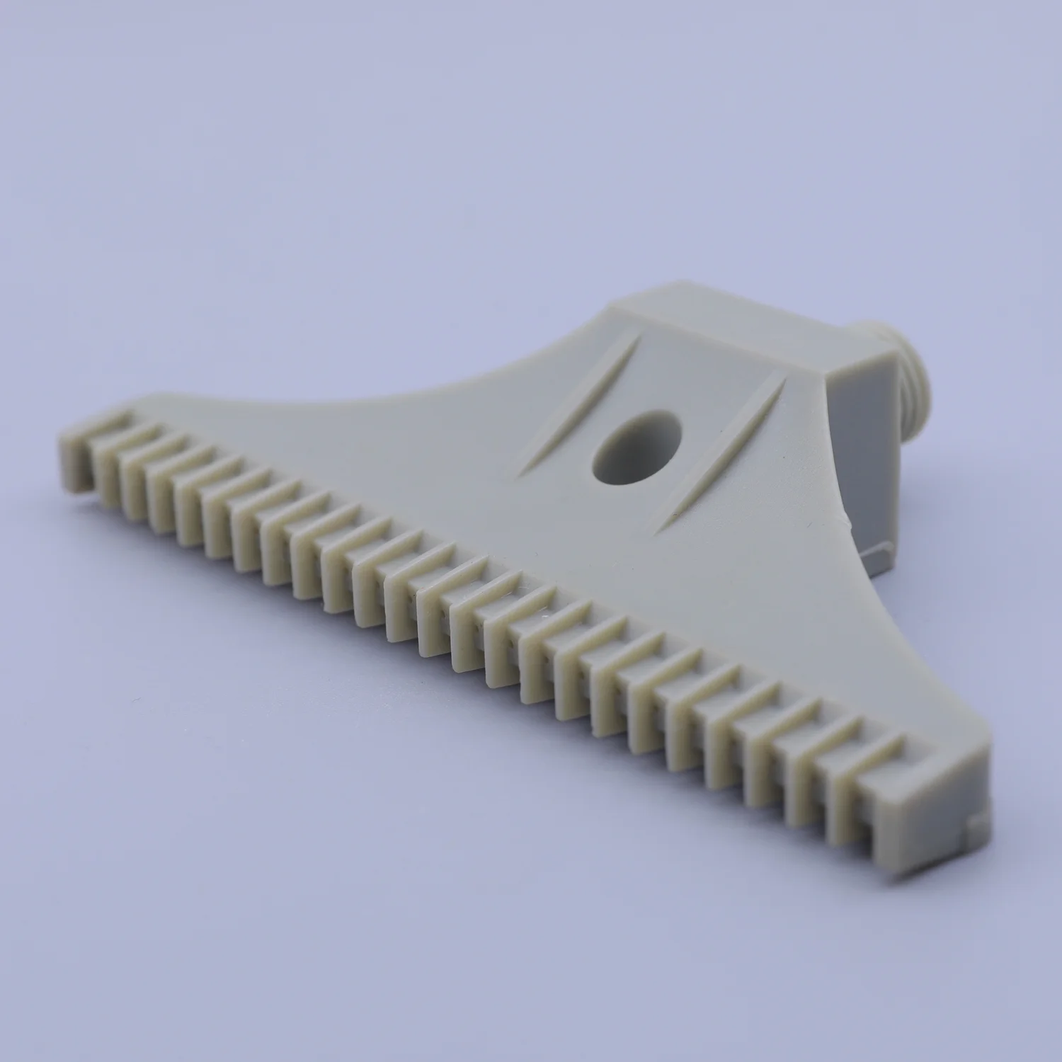 Beige plastic component with a comb-like edge and a cylindrical connector on a white background