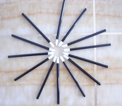 Disposable lip gloss brushes with white sponge tips and slim dark handles arranged in a fan