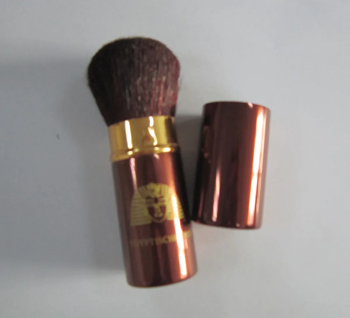 Retractable powder brush with a bronze aluminum tube gold ferrule and printed artwork shown with the cap removed