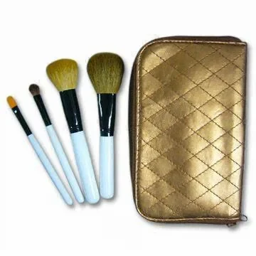 Set of four cosmetic brushes with pale handles beside a gold quilted zip pouch