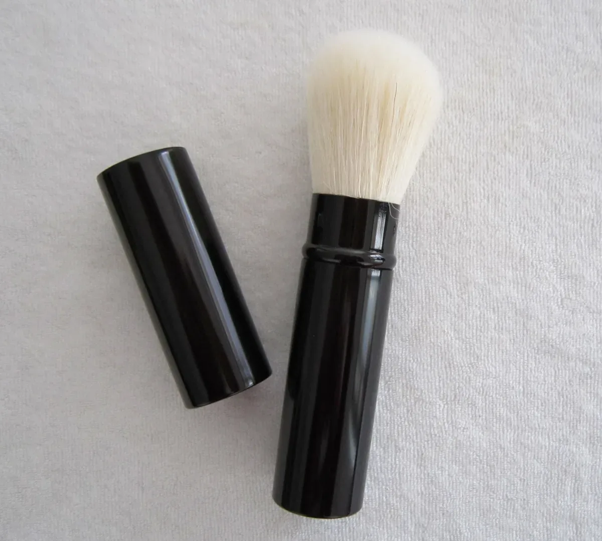 Compact retractable powder brush with white goat hair and a black aluminum tube