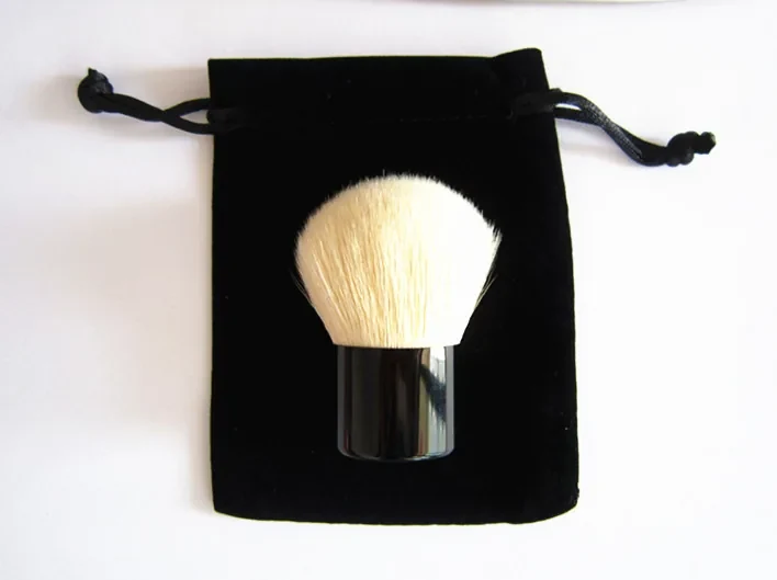 Goat hair kabuki brush with a black ferrule resting on a black drawstring pouch