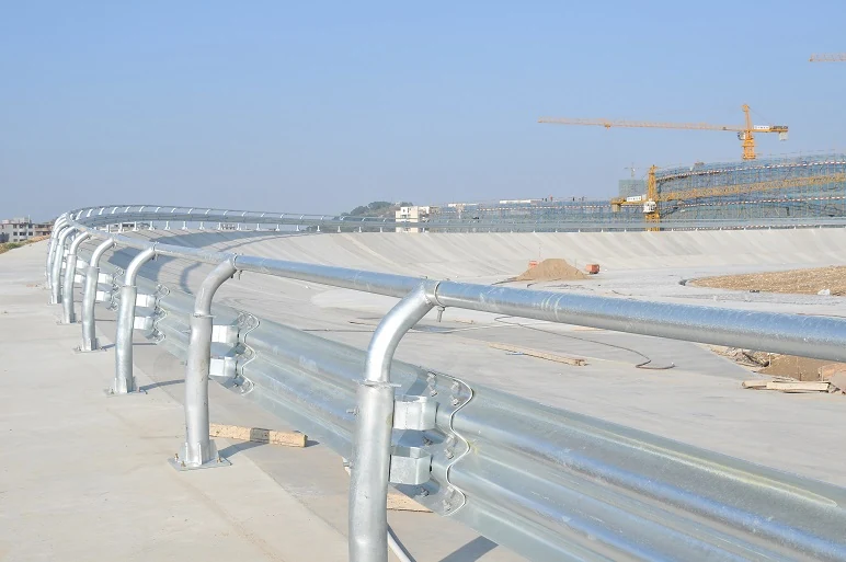 Galvanized W-beam guardrail curving along a concrete bridge, construction cranes visible in the background