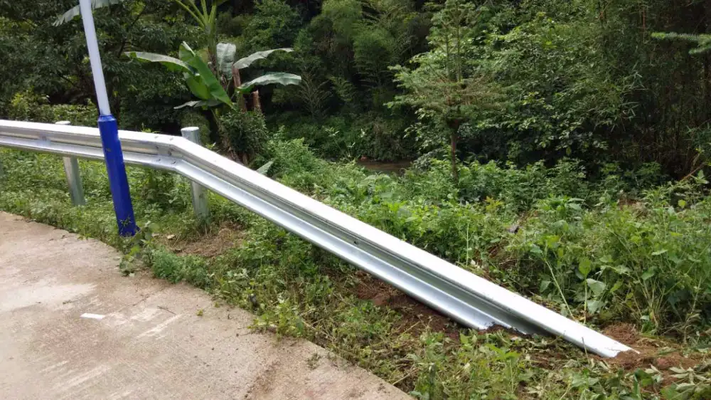 Galvanized W-beam highway guardrail on posts along a roadside edge with dense green vegetation behind