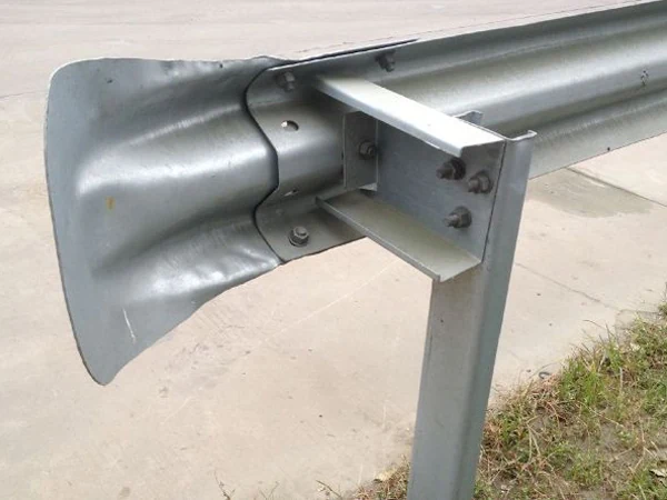 Galvanized steel guardrail end terminal with flared impact head bolted to W-beam rail on steel post over concrete