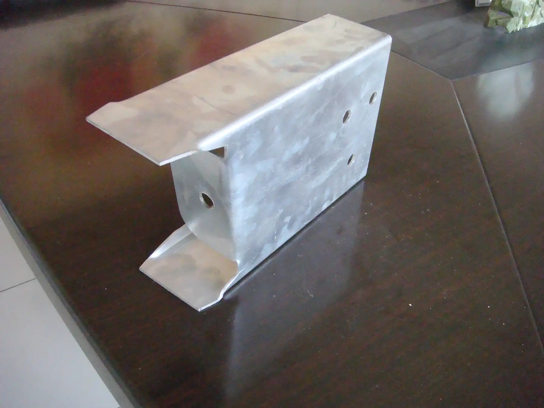 Galvanized steel bracket with pre-drilled holes photographed on a dark wooden table