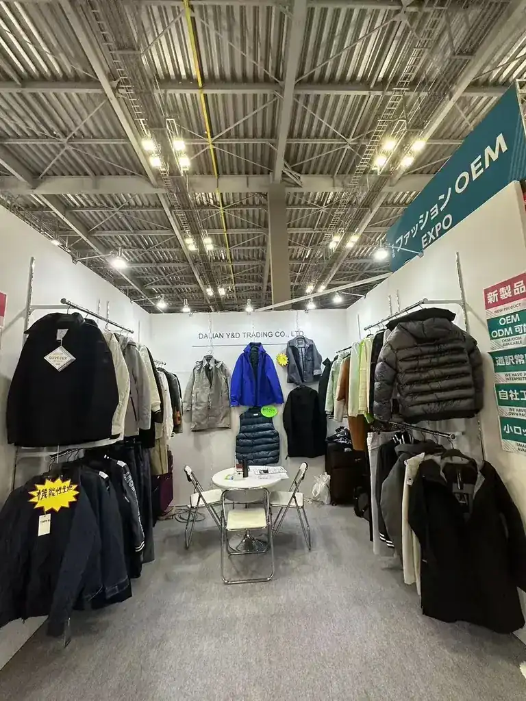 A second view of the trade fair booth showing shells, down jackets and knitted pieces on both walls