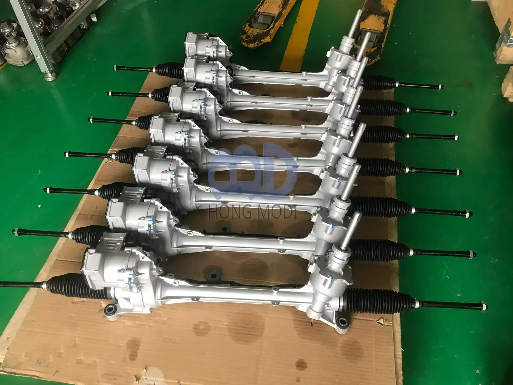 Electric power steering racks lined up in order on a green workshop pallet