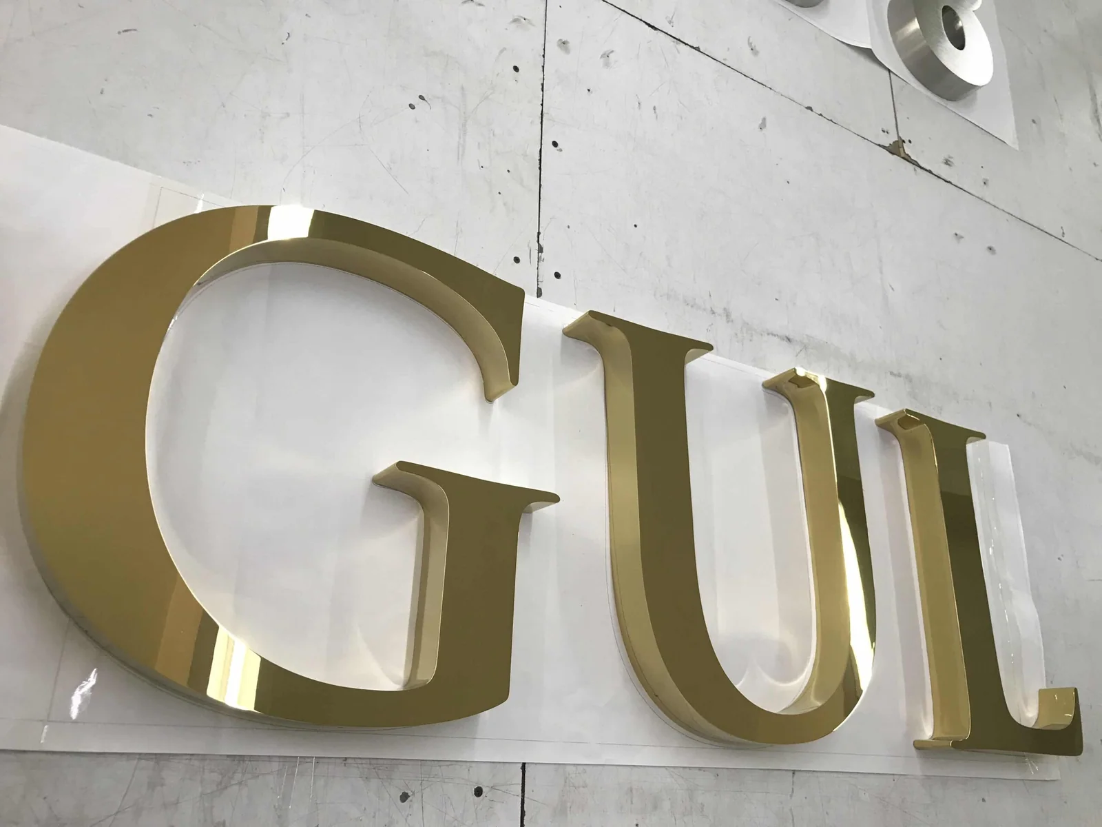Polished gold-finish flat-cut letters fixed to a bare concrete facade