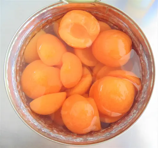 Open tin can of apricot halves in syrup, viewed from above
