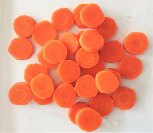 Round slices of fresh carrot scattered on a plain white surface