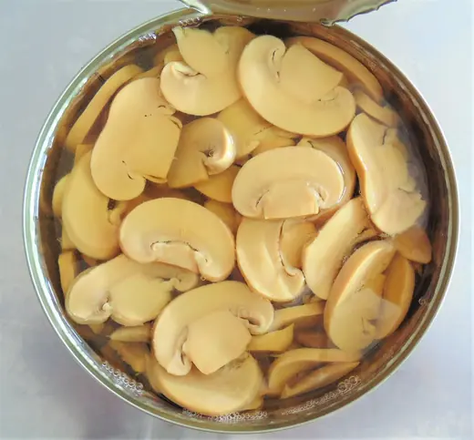 Top view of an open can filled with sliced mushrooms in brine