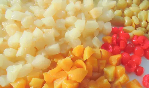 Close-up of diced mixed fruit including peach, pear, and cherry pieces on a white surface