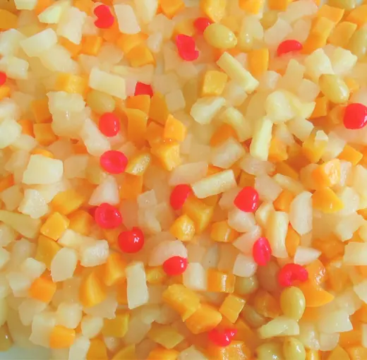 Diced mixed fruit cocktail with peach, pear, pineapple and red cherries filling the entire frame