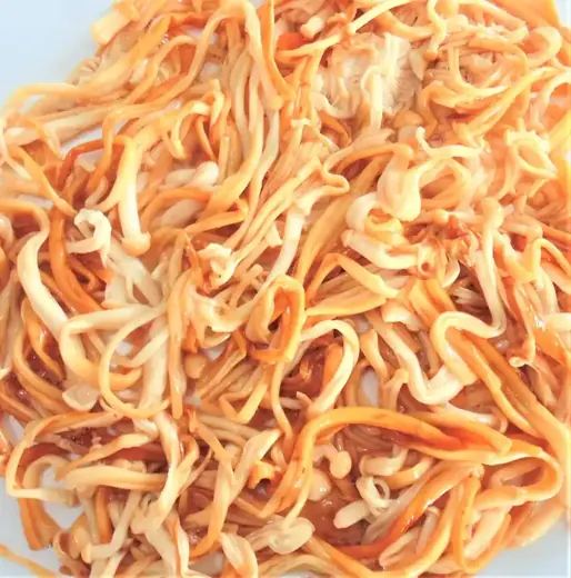 Close-up of seasoned shredded enoki mushrooms coated in orange chili sauce on a white plate