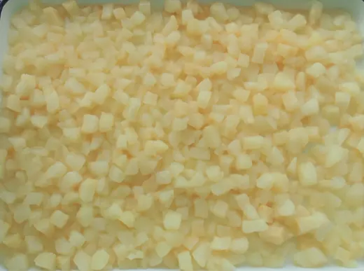 Overhead close-up of diced pale yellow fruit or vegetable pieces spread across a tray