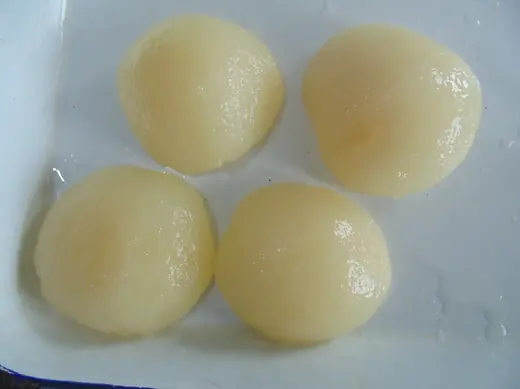 Four peeled pale-yellow pears with glossy wet surfaces arranged on a white tray