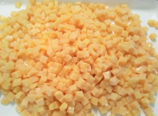 Close-up of small diced yellow-orange vegetable or fruit cubes spread across a white surface
