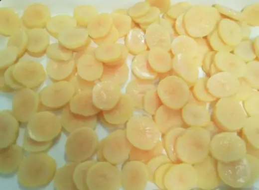 Round pale yellow vegetable slices arranged closely on a white surface