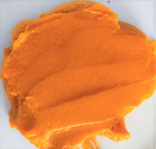 Close-up smear of smooth orange paste spread on a plain white surface