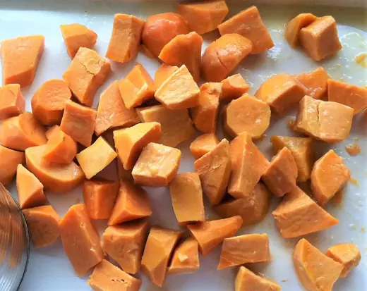 Cut chunks of raw orange sweet potato scattered on a white cutting board