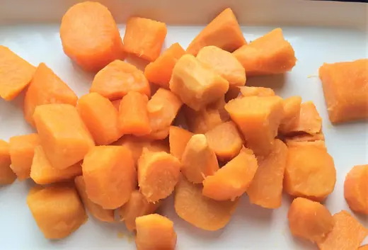 Pile of chopped orange carrot chunks on a white plate, close-up view