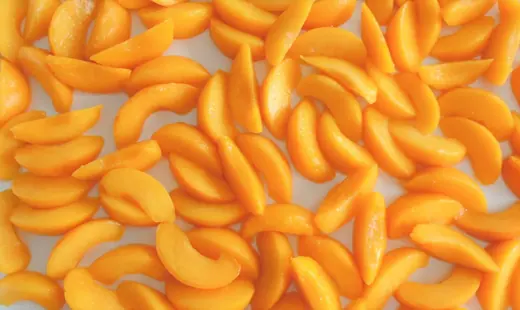Yellow peach slices tightly packed across the frame on a plain white background