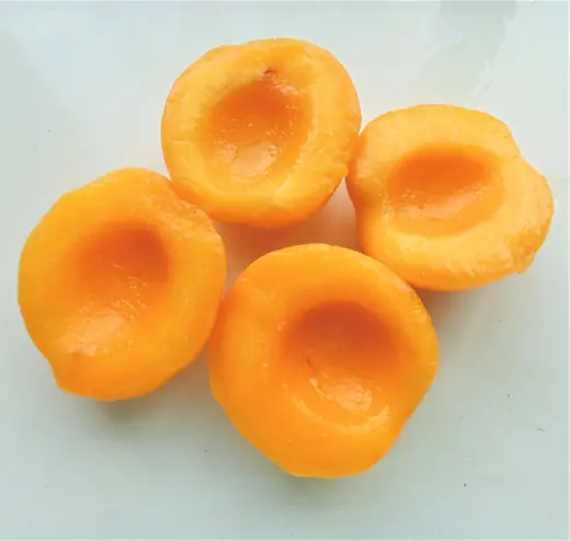 Four pitted yellow peach halves, glossy and syrup-coated, arranged on a plain white surface