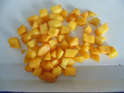 A pile of diced yellow fruit on a white cutting board