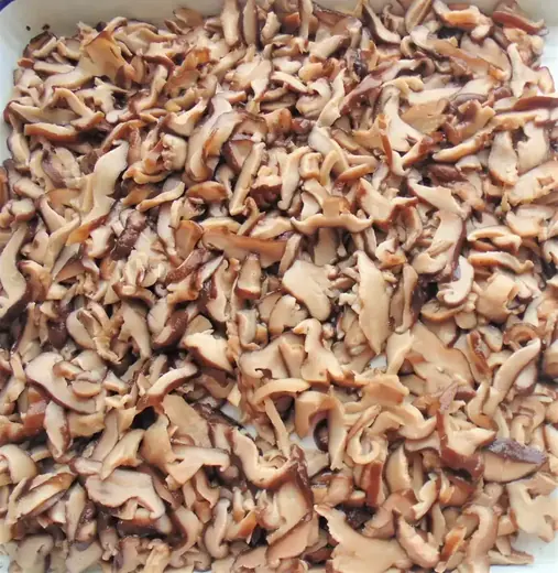 Sliced shiitake mushrooms piled in a white tray or container