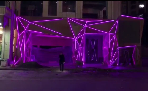 Angular park pavilion structure outlined in magenta linear lighting