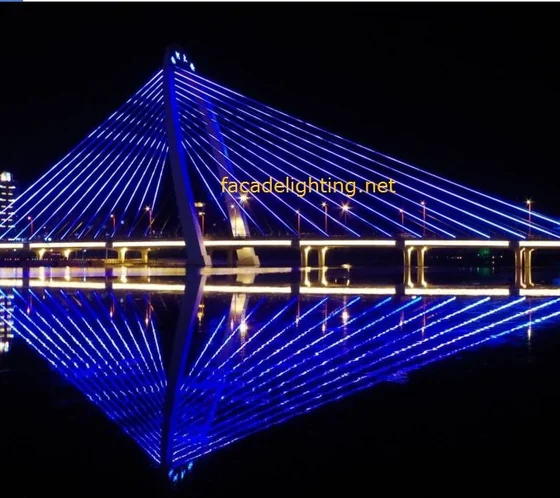 Cable stayed bridge lit with blue LED pixel light rays reflected in the river