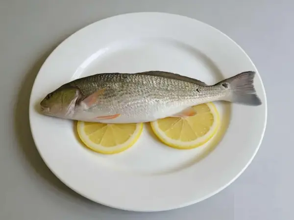 Whole red drum fish plated with lemon showing its tail spot marking