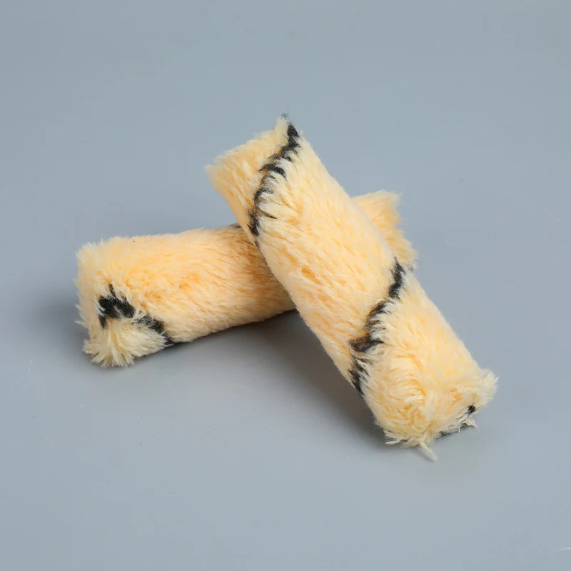 Two cream fabric paint roller covers with dark stripe lying crossed on a plain gray background