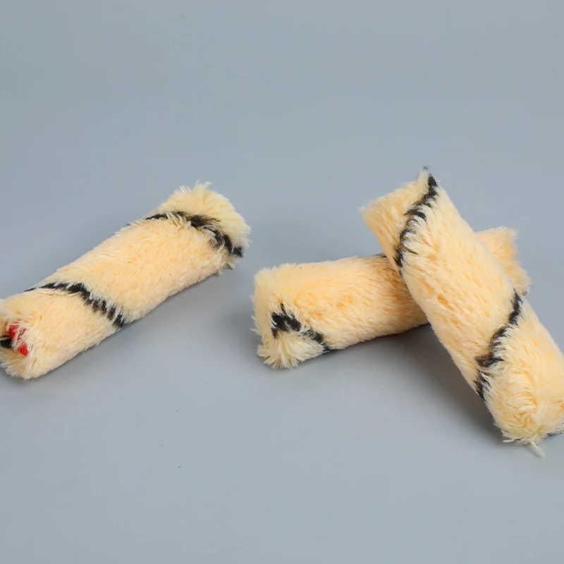 Three cream fabric paint roller covers with dark stripes lying on a plain gray-blue background