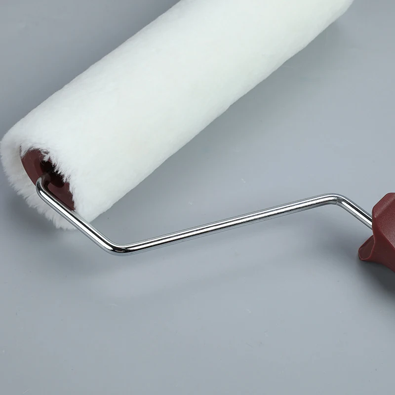 White fabric paint roller on a chrome wire frame with dark red grip, photographed on a plain gray background