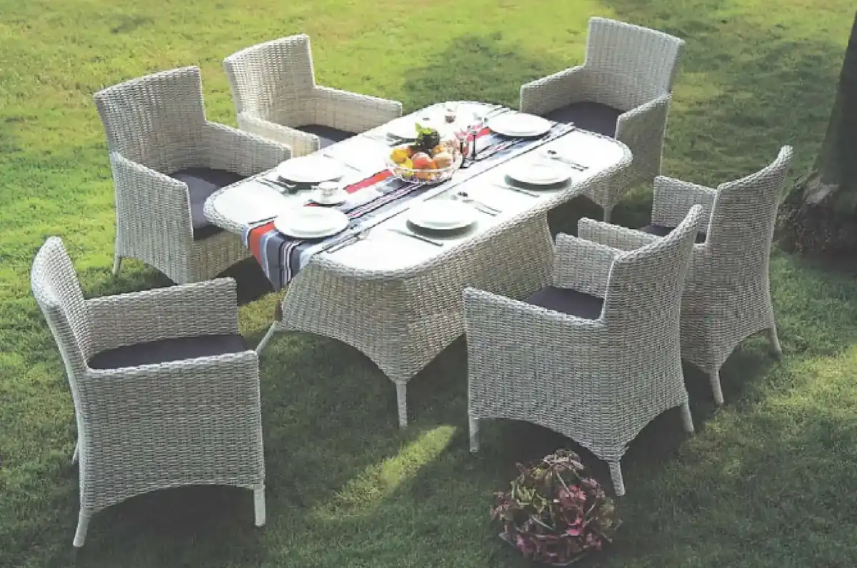 White synthetic rattan outdoor dining table with six matching armchairs and seat cushions