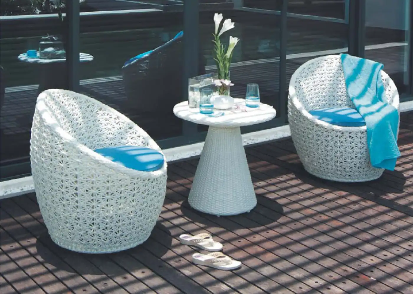 Two white woven rattan lounge chairs with blue cushions beside a small round side table on an outdoor wooden deck