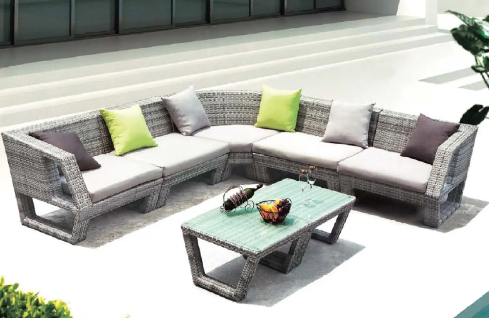 Gray wicker outdoor sectional sofa with cushions and matching glass-top coffee table on a white terrace