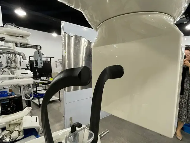 Detail view of the Carestream CS 9300 Select patient positioning system — two shaped rubber grip handles in black, the chin-rest cradle with clear bite-block holder, stainless-steel chin-positioning pin, and the glossy white chassis housing the generator column