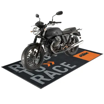 Motorcycle parked on a printed race pit mat with orange and grey graphics