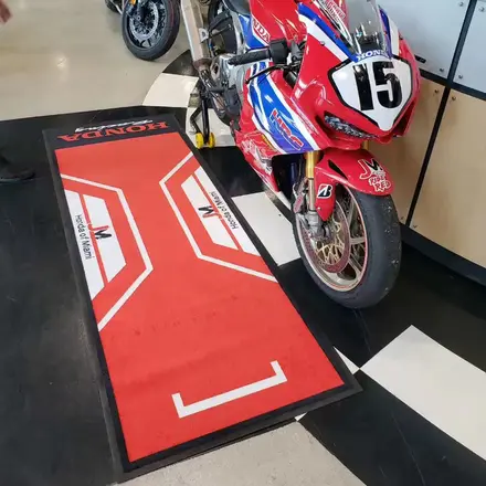 Red custom printed pit carpet with a dealership logo under a motorcycle