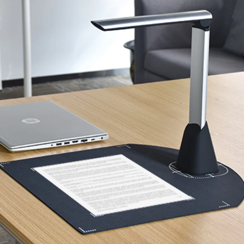 Overhead document scanner capturing a page on an office desk beside a laptop