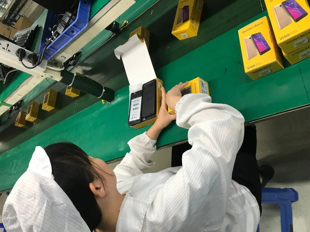 An operator checking a Golden Berry handset against the packing sheet before the retail box is closed