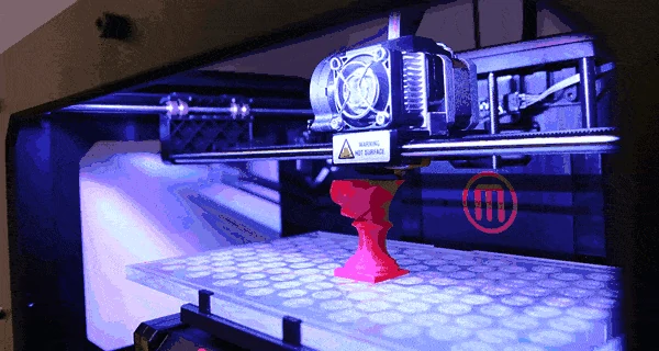 3D printer extruder building a part in a darkened print chamber