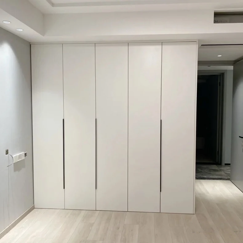 Full height white fitted wardrobe run with slim vertical handles in a finished bedroom