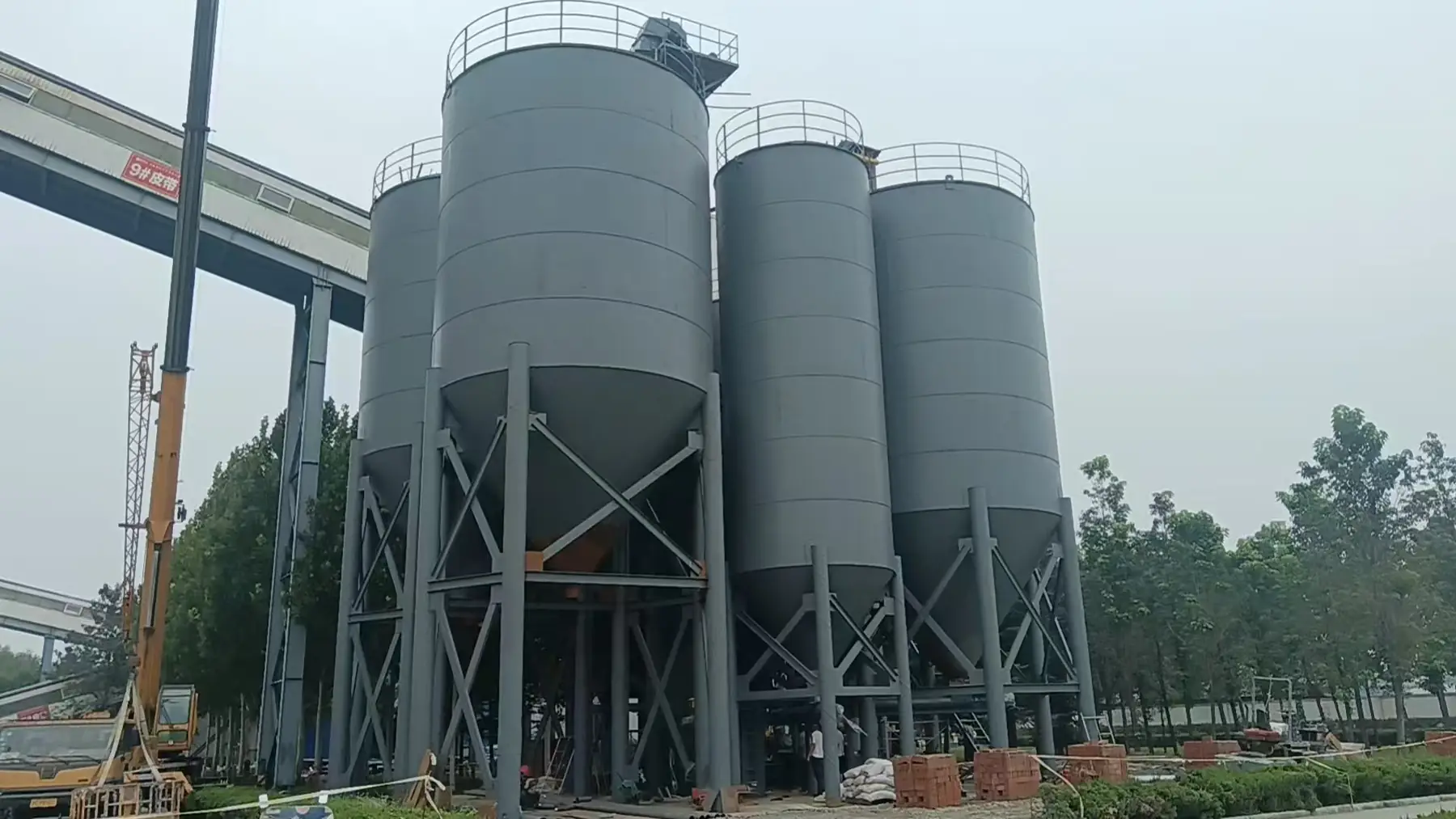 Steel silo battery under erection on a concrete foundation with a crawler crane on site