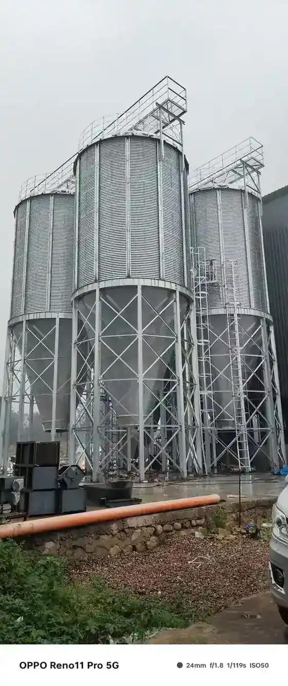 Cone bottom feed granary standing on steel legs beside a farm building
