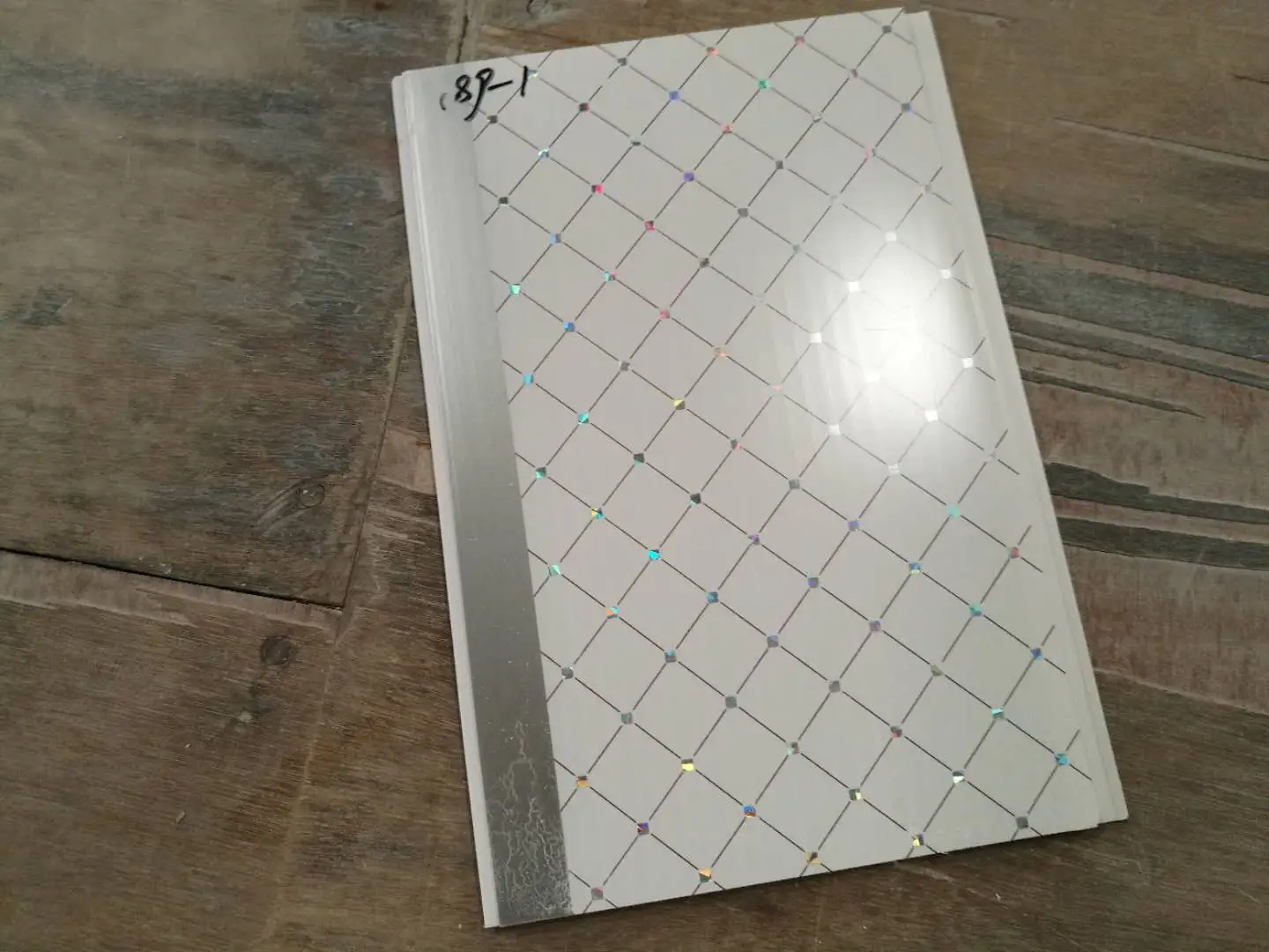 A white decorative panel with a diamond grid pattern and a silver edge, resting on a wooden surface.